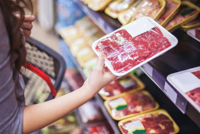 A person holding wrapped meat in a grocery store